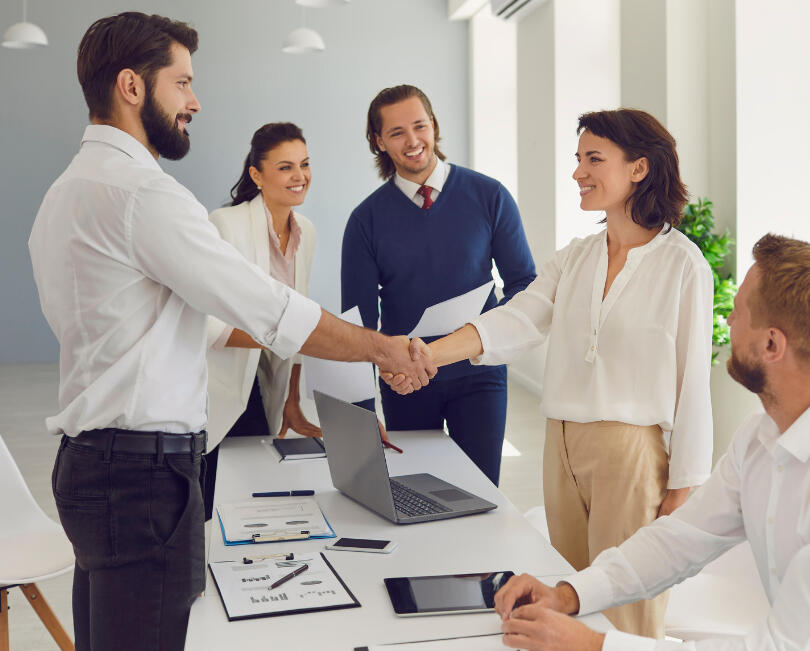 Women and man dressed as smart business people shaking hands surrounded by other business people